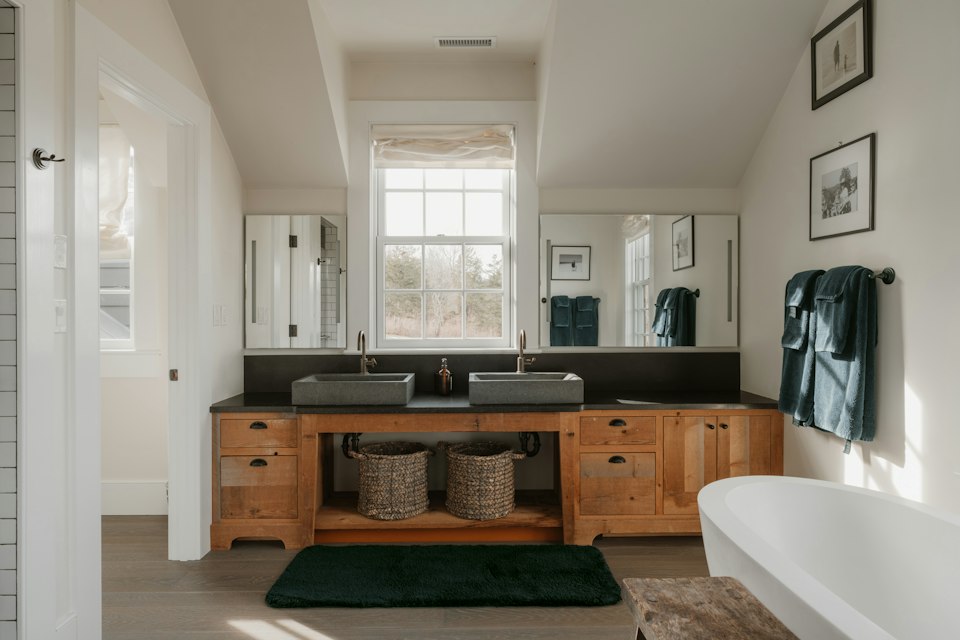 Bathroom with a wooden double vanity, two vessel sinks, a window and a freestanding tub