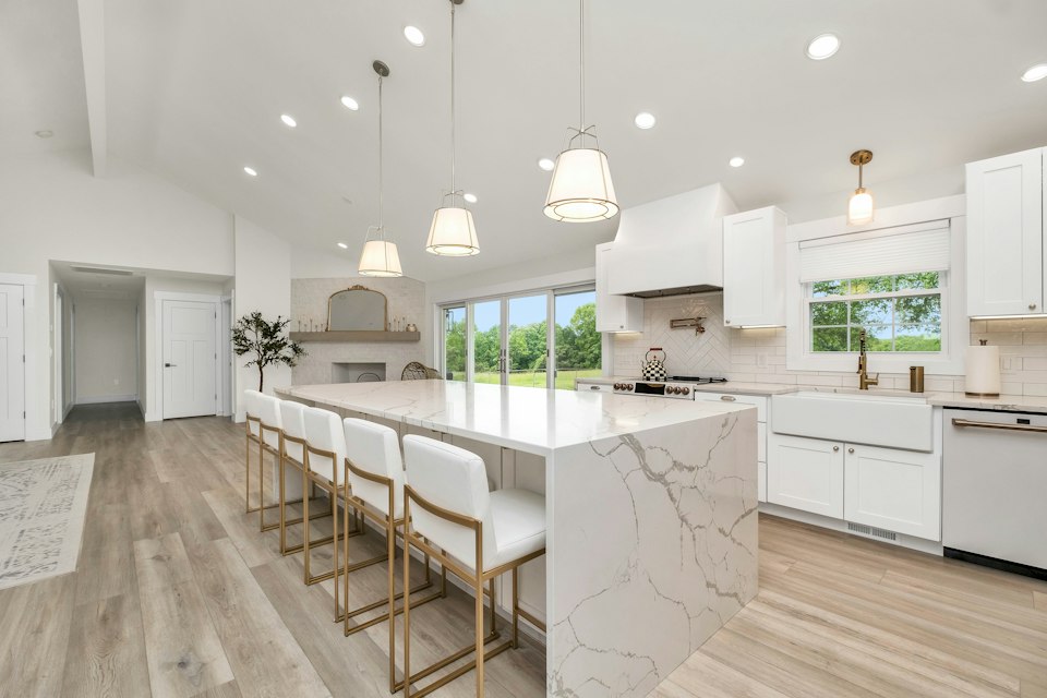 Bright kitchen with a long marble-look island, white bar stools, pendant lights and white cabinets