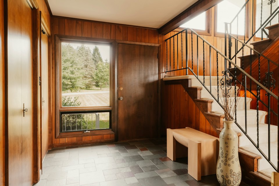 Entry area with a slate tile floor, wood-paneled walls, a bench, a window to the yard and stairs
