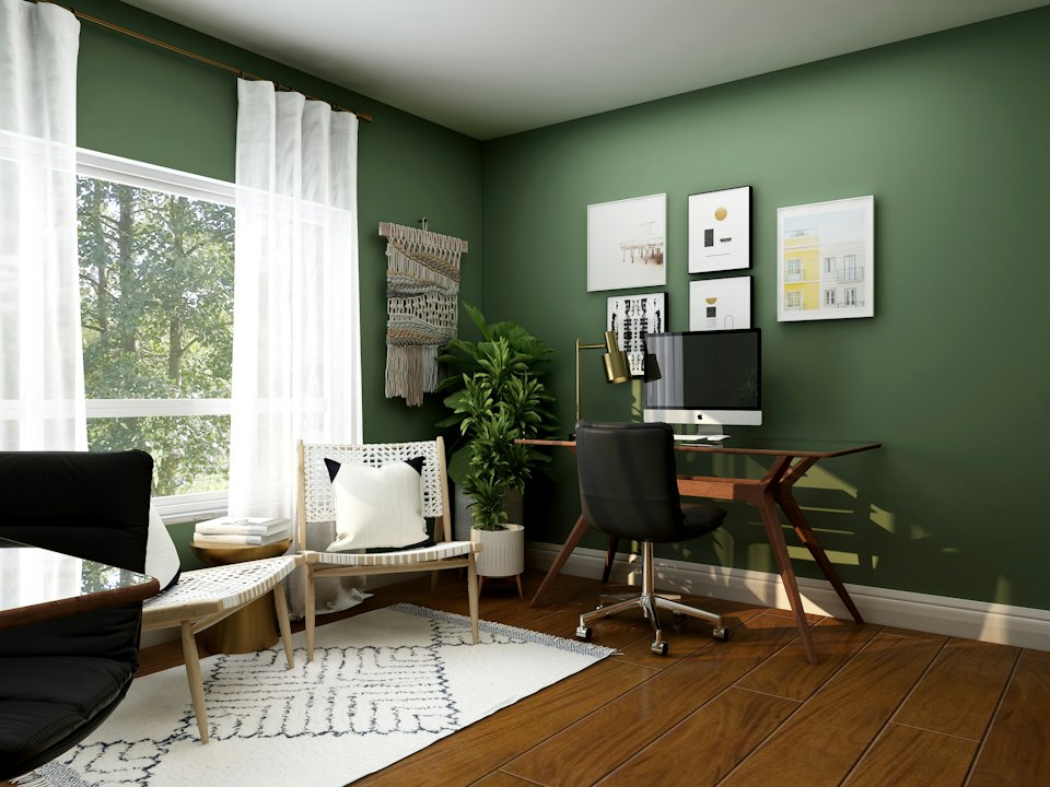 Office with green walls, a wooden desk with a computer, a large curtained window and an armchair