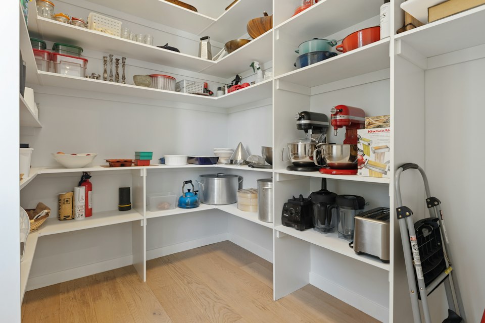 Walk-in pantry with white shelves on three sides holding cookware, small appliances and dry goods