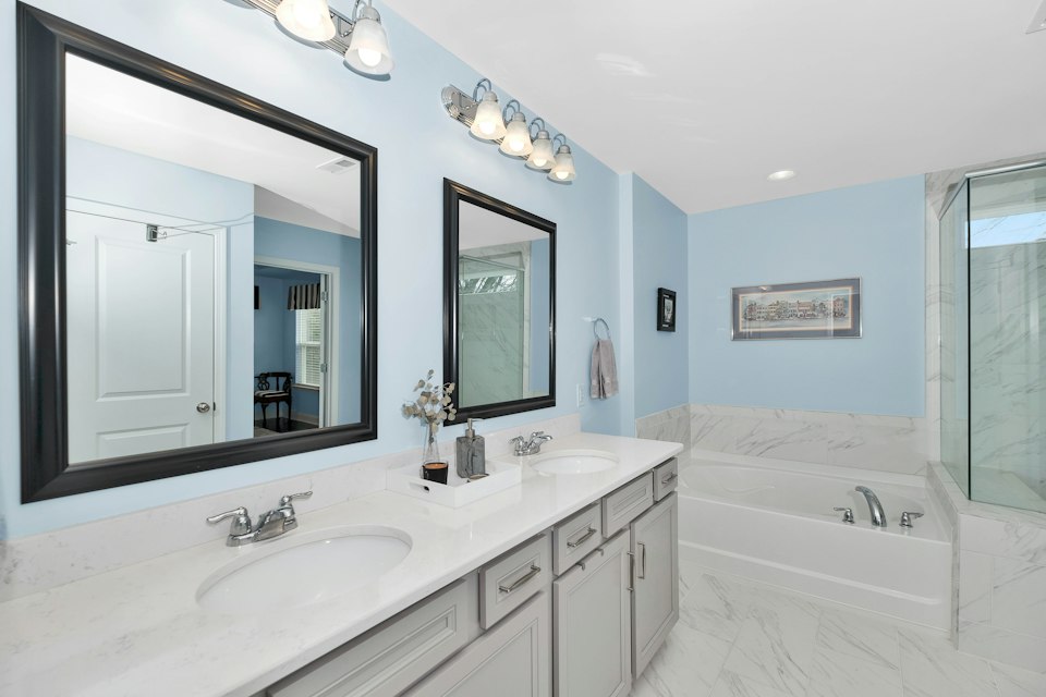 Bathroom with light blue walls, a double-sink vanity with two mirrors, a soaking tub and a glass shower