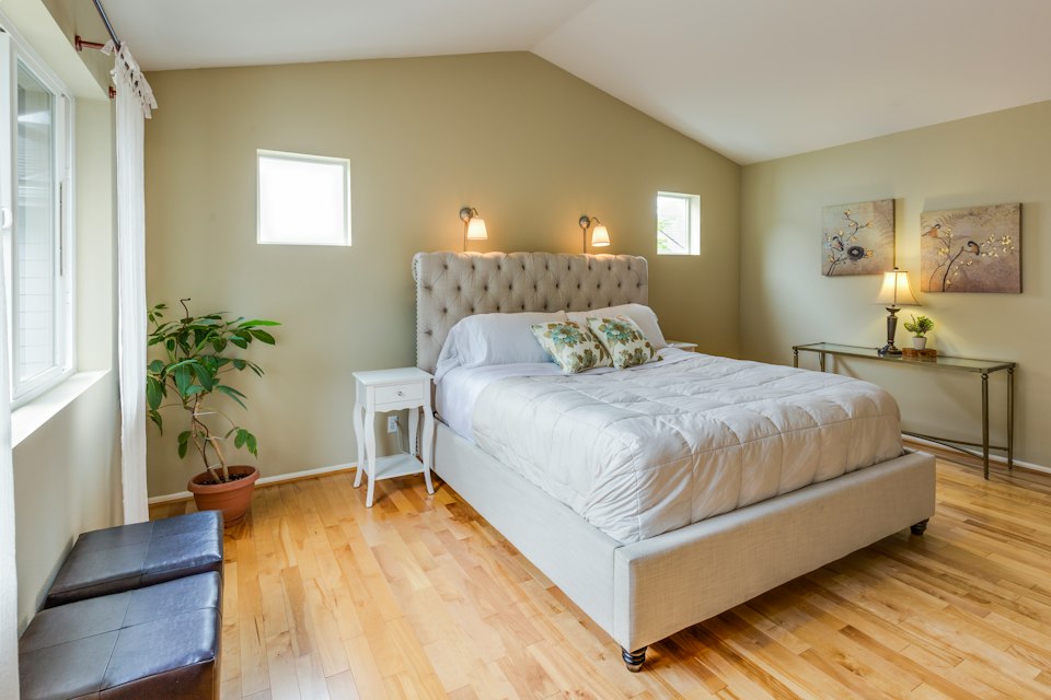 Bedroom with a sloped ceiling, a tufted upholstered bed, light wood floors and small windows