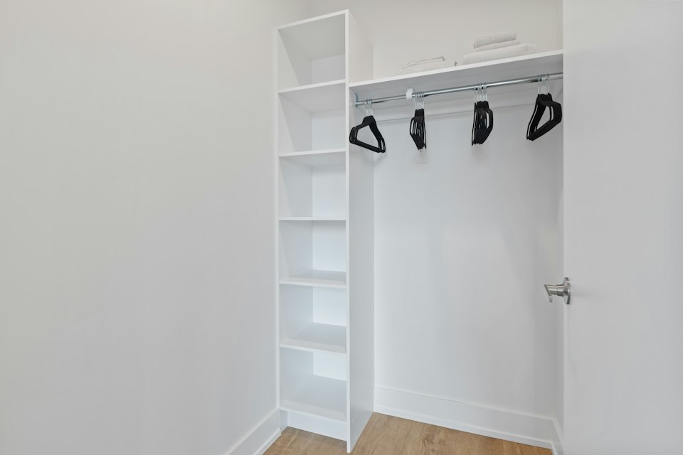 Walk-in closet with white shelves and a hanging rail with black hangers